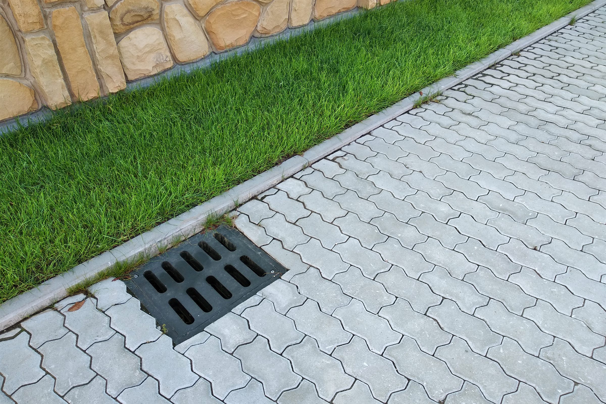 Drain grate set into a paver driveway beside a strip of lawn