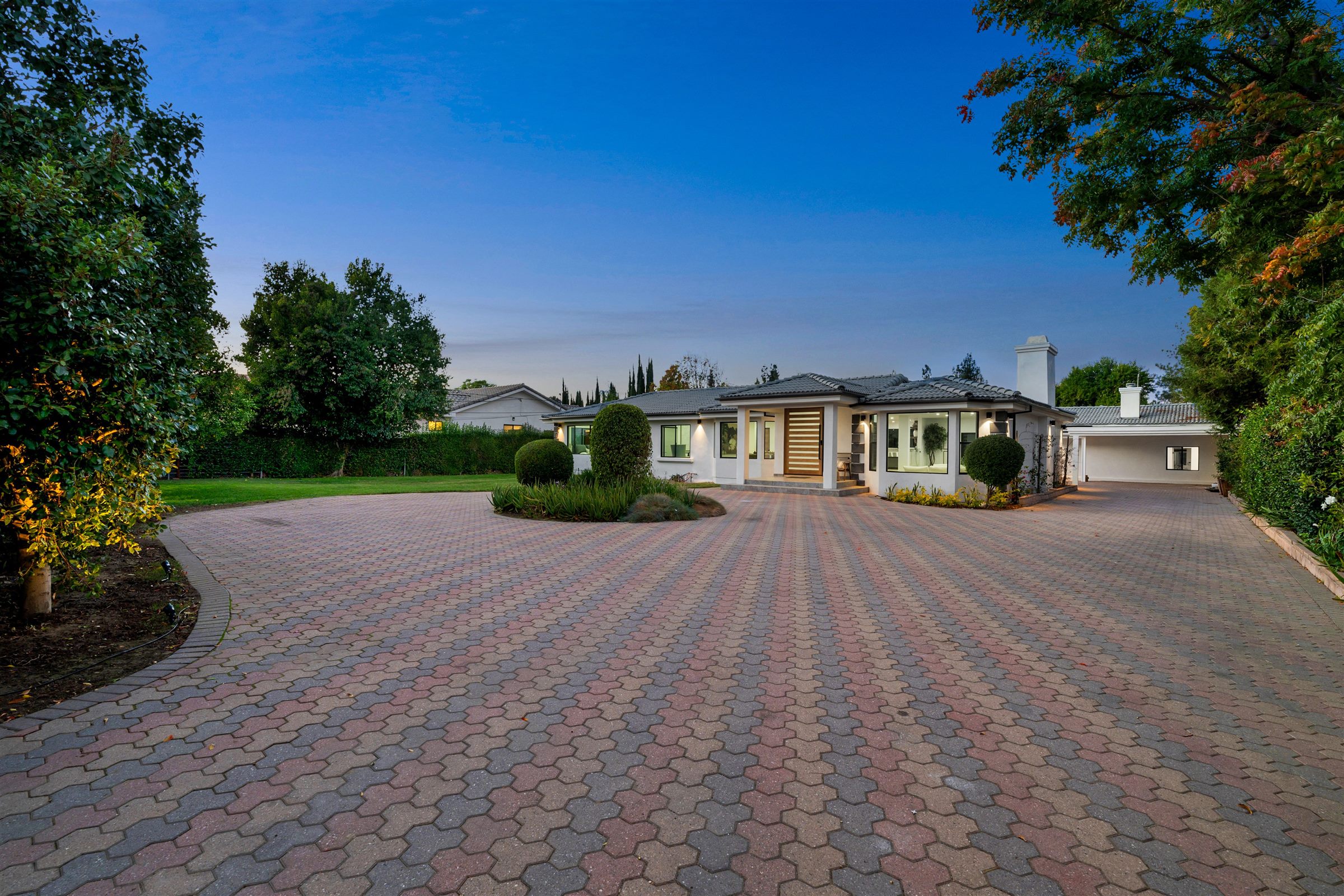 Wide curved paver driveway leading to a single-story home at dusk