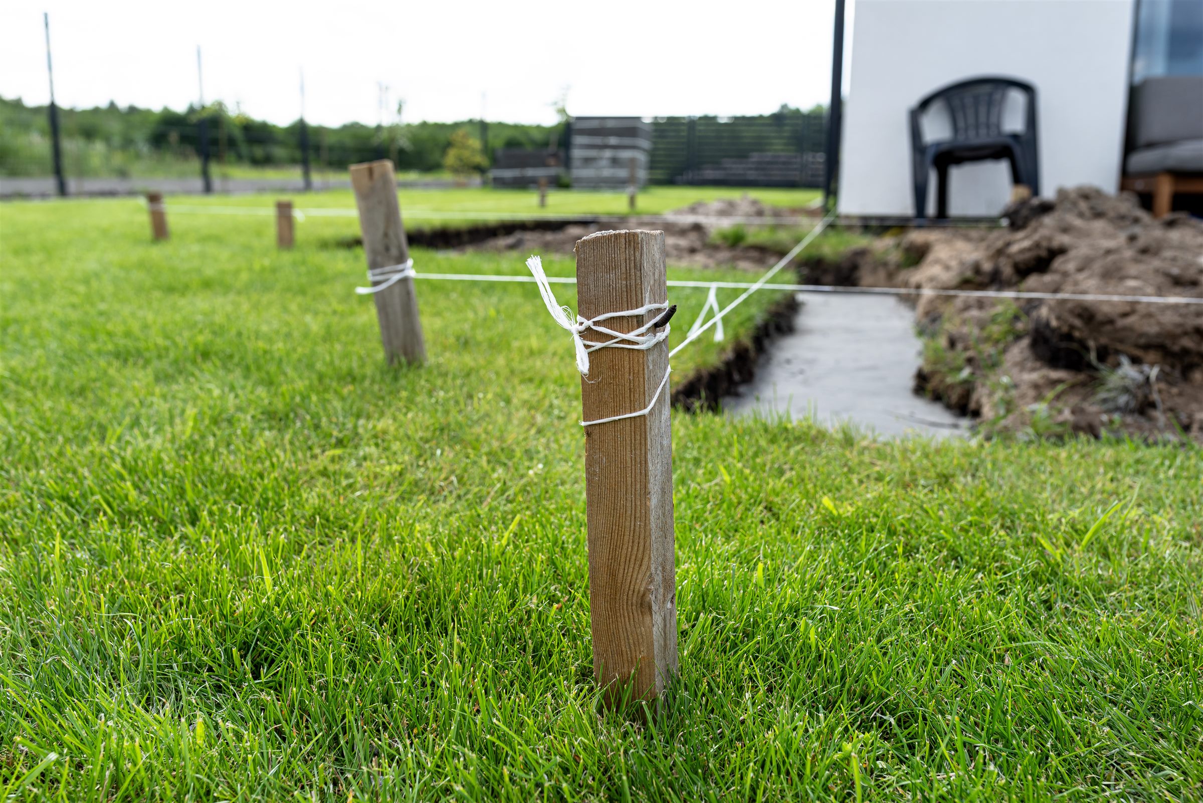 Wooden stakes and string marking a layout line across a lawn
