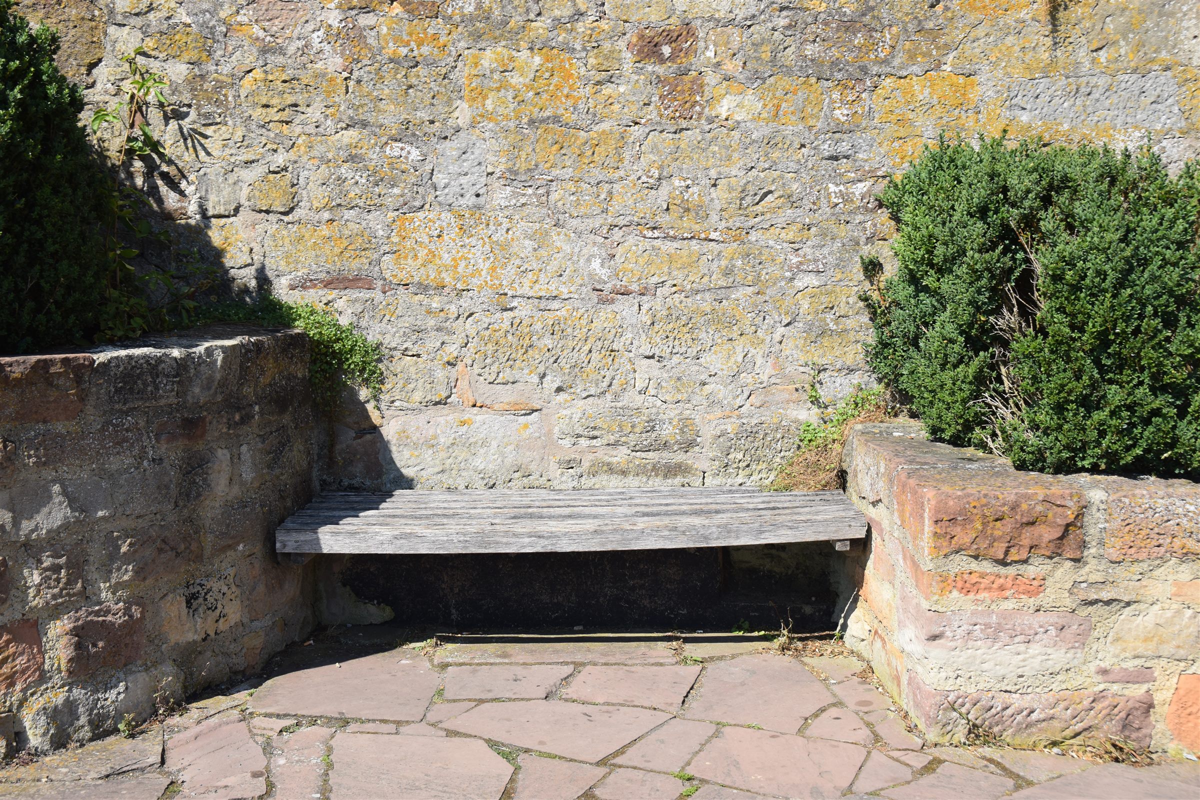 Wooden bench built into a stone wall beside a flagstone patio